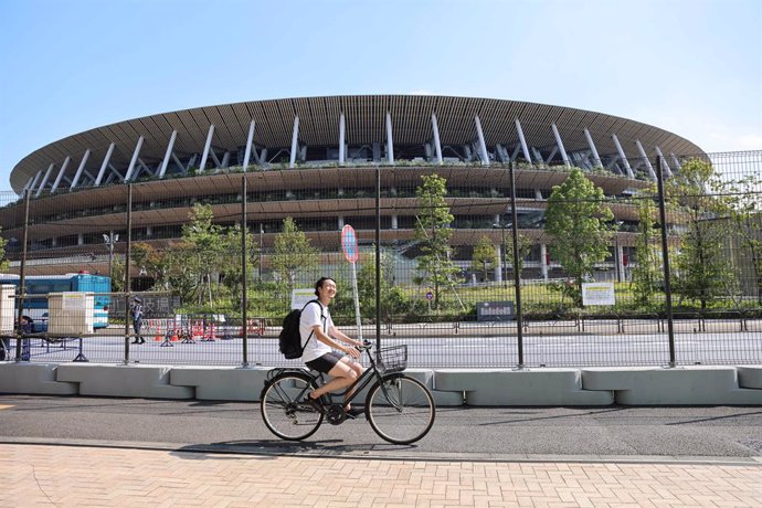 19 July 2021, Japan, Tokyo: A man rides a bike past a security fence surrounding the National Stadium in Shinjuku, ahead of the 2020 Olympic Games. Tokyo 2020 Olympic Games will be held from 23 July to 8 August 2021. Photo: Stanislav Kogiku/SOPA Images 