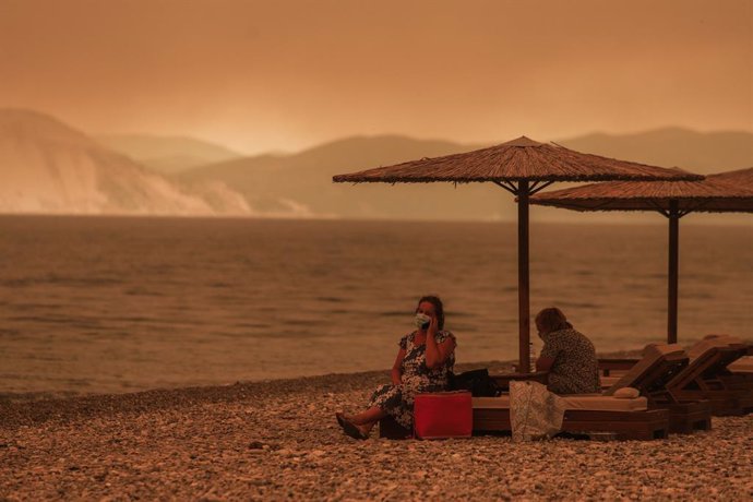 08 August 2021, Greece, Gouves: Two people sit on deck chairs on a smoke-shrouded beach near the village of Gouves on the island of Euboea. Photo: Eurokinissi/Eurokinissi via ZUMA Press Wire/dpa