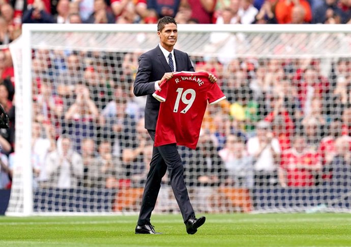 14 August 2021, United Kingdom, Manchester: Manchester United's Raphael Varane holds up his shirt on the pitch as is is confirmed that he has signed for the club on a four-year deal ahead of the English Premier League soccer match between Manchester Uni