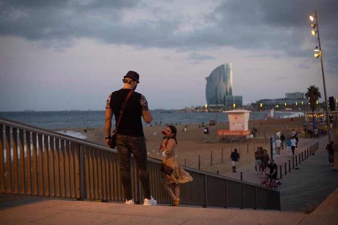 Un home fa fotos a una dona enfront de la platja de la Barceloneta, a 4 d'agost de 2021, a Barcelona, Catalunya (Espanya). Barcelona afronta aquest estiu una temporada turística marcada per la cinquena ona de la pandmia per Covid-19 a Espanya, que ha re