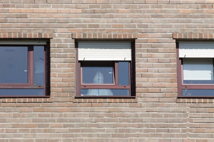 Un trabajador sanitario con un EPI, en la ventana de una habitación de una residencia 