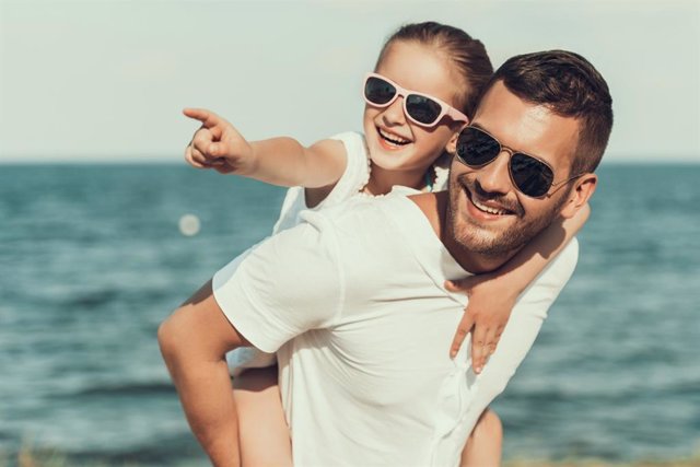 Padre y su hija paseando por la playa en verano con gafas de sol.