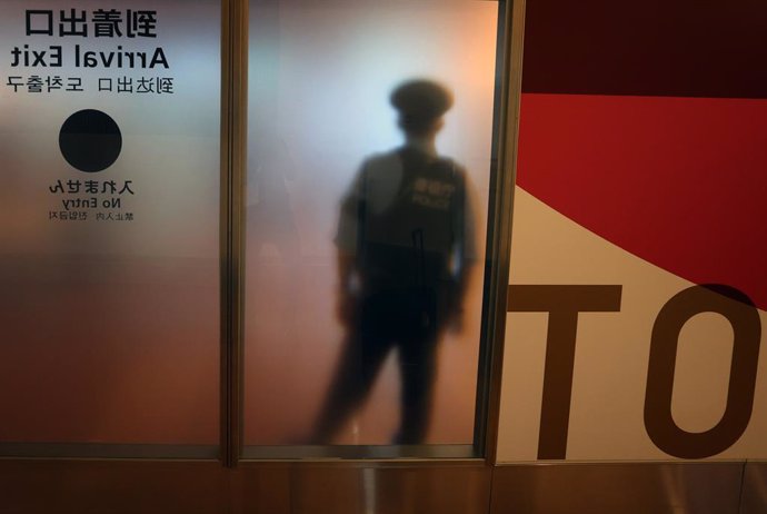 22 August 2021, Japan, Tokyo: A police officer stands in front of a frosted glass window at an exit for air travelers at Haneda Airport. Photo: Karl-Josef Hildenbrand/dpa