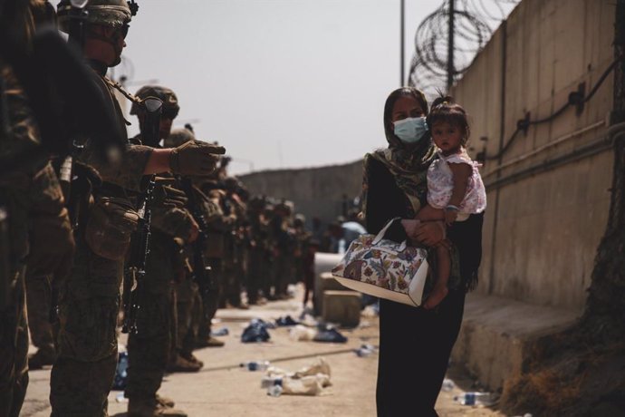 18 August 2021, Afghanistan, Kabul: 2 Marines from the 24th Expeditionary Unit (MEU) guide a woman carrying a child in her arms during an evacuation at Hamid Karzai International Airport in Kabul. US soldiers and Marines are assisting the State Departme