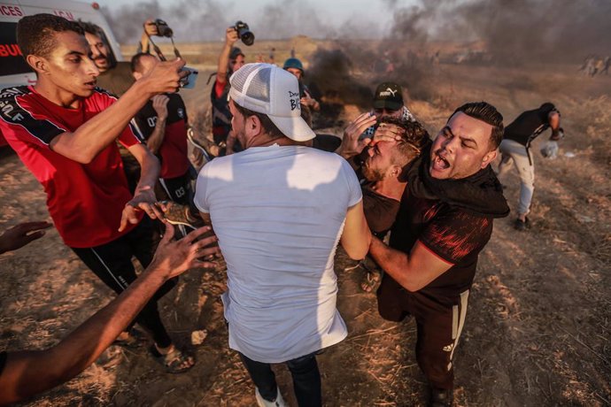 25 August 2021, Palestinian Territories, Khan Yunis: Palestinian demonstrators carry an injured man during a protest along the border fence, east of Khan Yunis in the southern Gaza Strip denouncing the Israeli blockade of the Palestinian sector. Photo: 