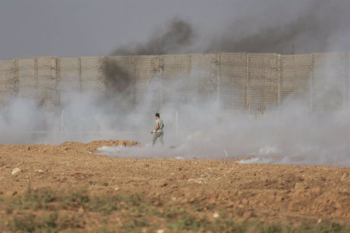 21 August 2021, Palestinian Territories, Gaza: A Palestinian protester runs away as tear gas canisters shot by Israeli security forces from across the Gaza border fall following a demonstration, denouncing the Israeli siege of the Palestinian strip. Pho