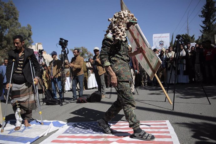 Archivo - Un soldado houthi camina sobre una bandera estadounidense durante una protesta frente a la embajada de Estados Unidos en Saná.