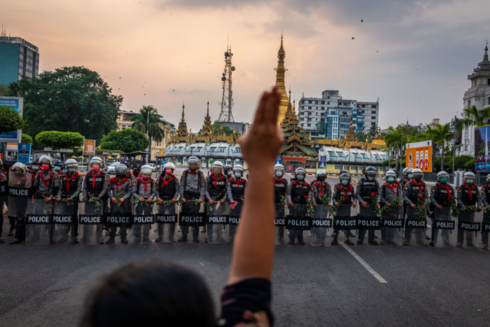 Un manifestante hace un saludo de tres dedos frente a una fila de policías antidisturbios, que sostienen rosas que les dieron los manifestantes, el 6 de febrero de 2021 en Rangún, Birmania.