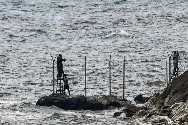 Archivo - Personas (al fondo), instalan una valla en la playa del Tarajal, a 24 de junio de 2021, en Marruecos. 