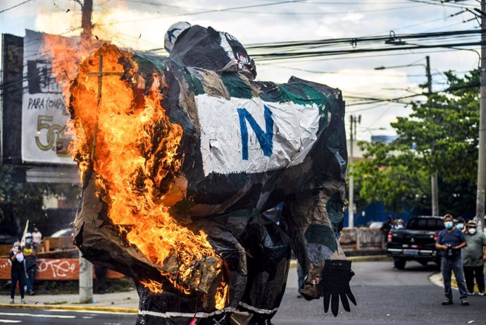 Archivo - 30 July 2021, El Salvador, San Salvador: A paper statue representing militarism is set on fire during a protest against the government of Salvadoran President Nayib Bukele on the 46th anniversary of a government led massacre against peacfully 