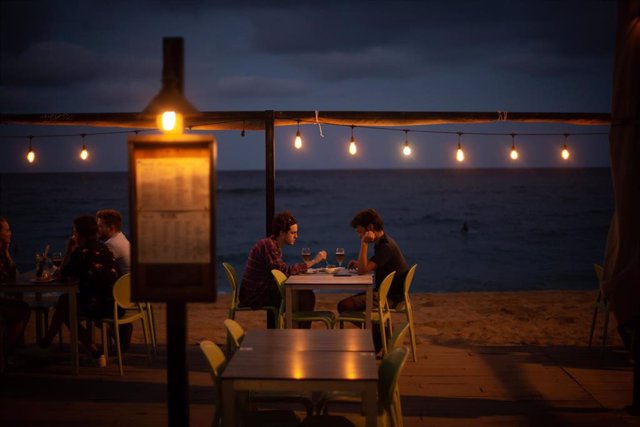 Dos jóvenes en la terraza de un restaurante, frente a la playa de la Barceloneta