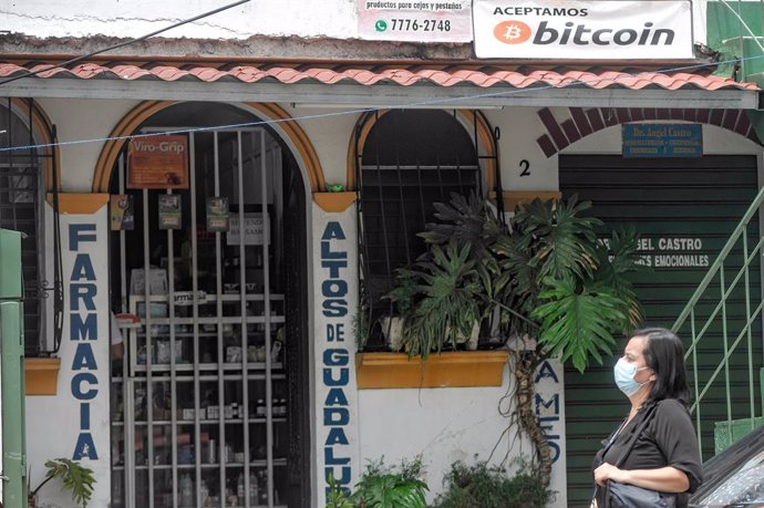 Archivo - 09 June 2021, El Salvador, San Salvador: A woman passes by a local business that accepts bitcoin as a payment method. El Salvador's Congress approved the digital currency Bitcoin as a legal tender, meanwhile, Salvadoran President Nayib Bukele 