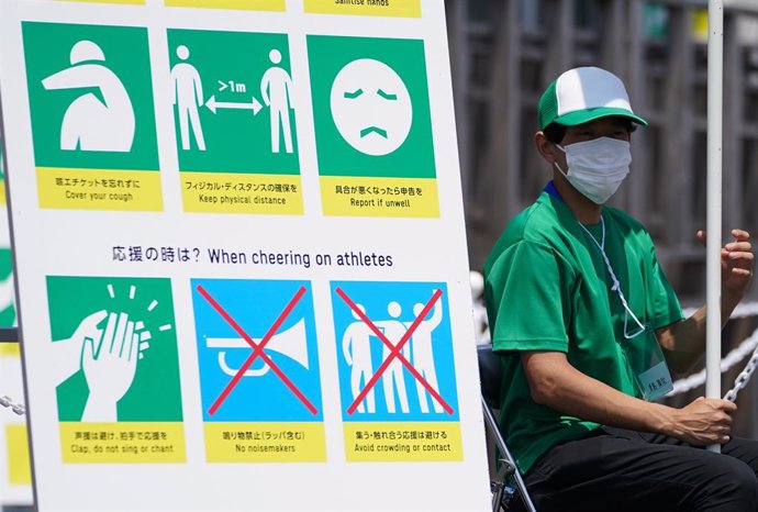 Archivo - 20 July 2021, Japan, Tokyo: A volunteer sits next to a sign warning of COVID-19 countermeasures ahead of the Tokyo 2020 Olympic Games set to place place between 23 July until 08 August 2021. Photo: Mike Egerton/PA Wire/dpa