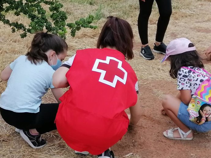 Una voluntaria de Cruz Roja planta semillas junto a unas niñas.
