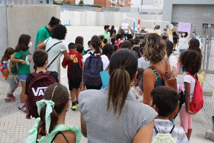 Alumnos acompañados por sus padres en la entrada de un colegio.