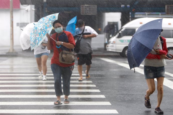 12 September 2021, Taiwan, Keelung: People hold umbrellas as they cross a cross-walk in Keelung as Typhoon Chanthu hits Taiwan with lasting effects on China and Japan. Schools and businesses have been closed in some parts of Taiwan to prevent injuries a