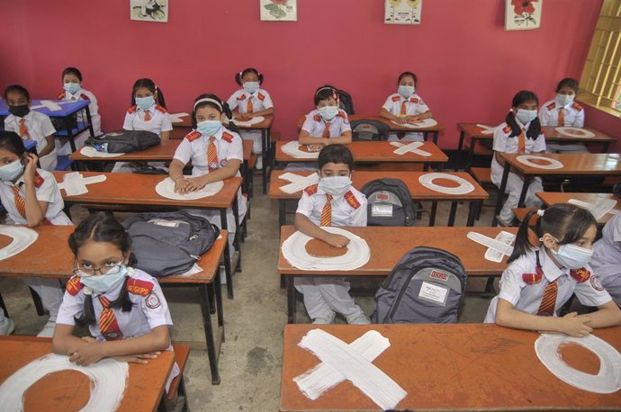 12 September 2021, Bangladesh, Sylhet: Students at Govt Kindergarten Elementary School sit in their classroom wearing medical masks and keeping their distance from each other, on the first day after the school was closed for 543 days because of the Coro
