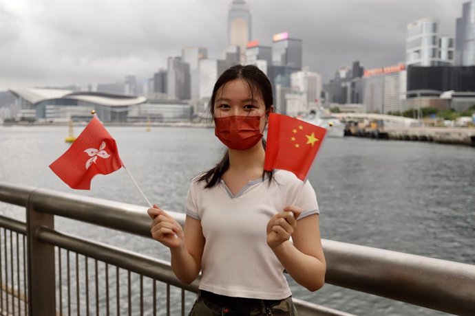 Archivo - 01 July 2021, China, Hong Kong: A young Chinese woman waves China's national flag and Hong Kong official flag as gesture of celebration at the Victoria Harbour waterfront on the morning of the 24th anniversary of Hong Kong's Handover and 100th
