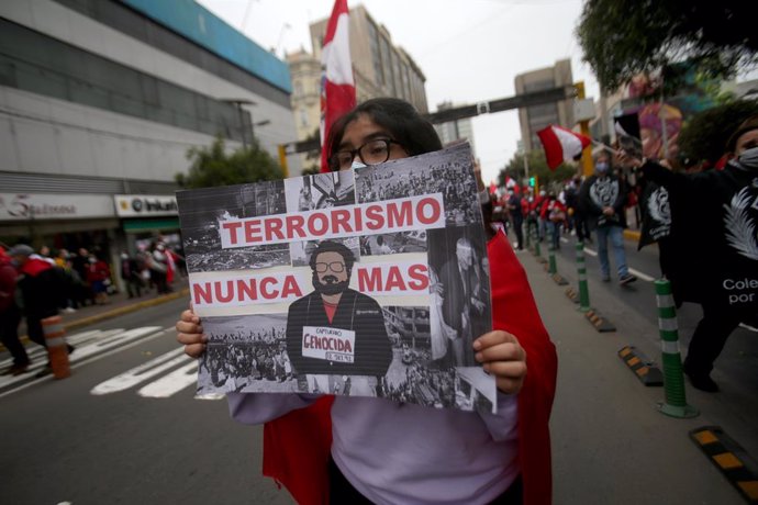 12 September 2021, Peru, Lima: A woman carries a placard describing Peruvian guerrilla leader Guzman as a mass murderer at a demonstration marking his death. Abimael Guzman, the former leader of the Peruvian guerrilla organization Shining Path (Sendero 