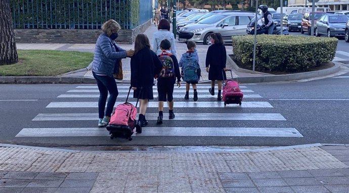 Varios alumnos con sus padres cruzan por un paso de peatones para acudir al colegio.