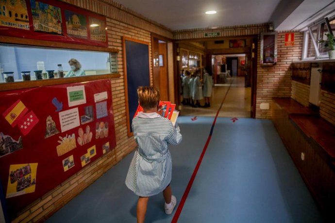 Un niño camina con libros por el hall de un colegio.
