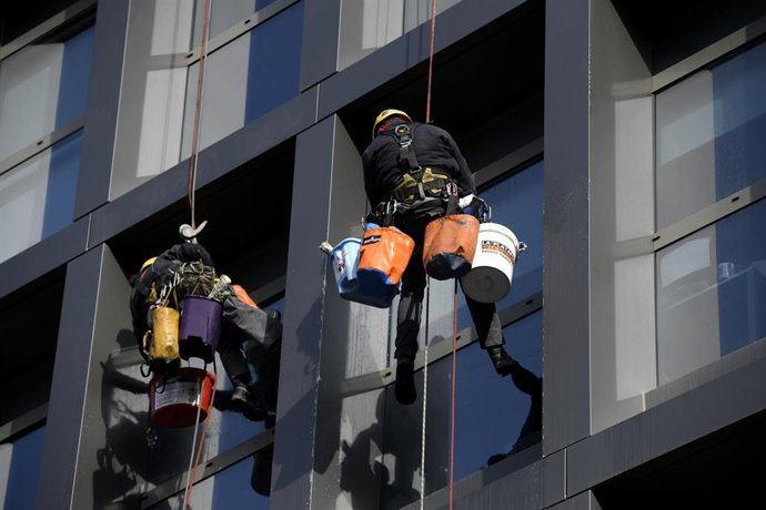 Archivo - Dos operarios limpian los cristales exteriores de un edificio.