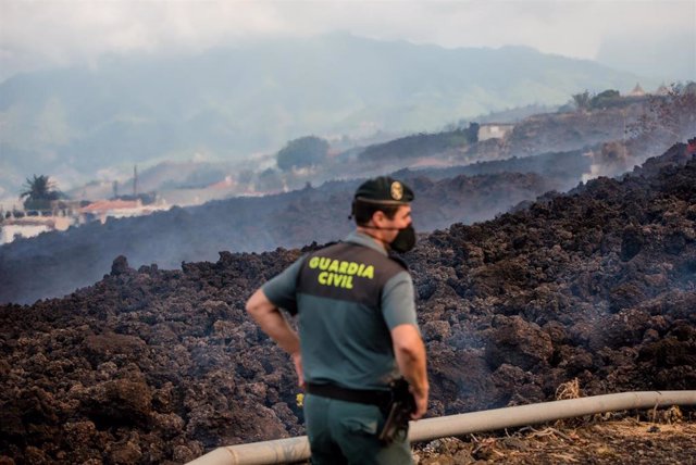 20 September 2021, Spain, El Paso: Smoke rises in front of a Guardia Civil official from cooling lava that has flowed over a road on the Canary island of La Palma. The volcano had become active again on Sunday for the first time in 50 years. Photo: Arturo