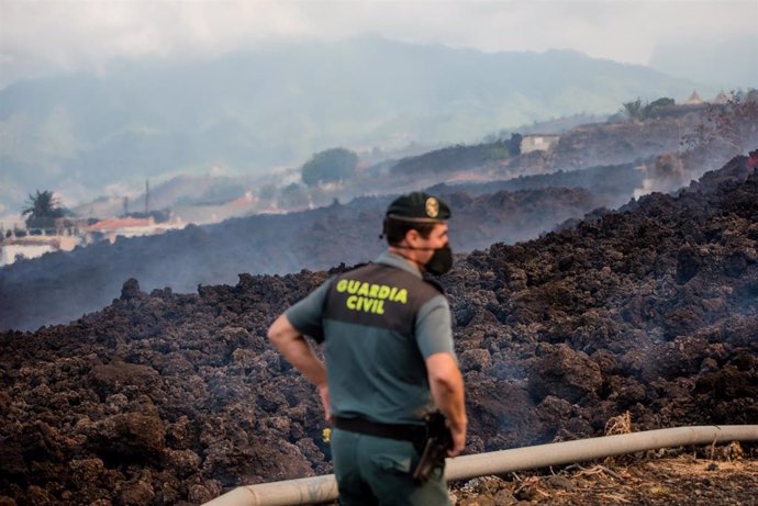20 September 2021, Spain, El Paso: Smoke rises in front of a Guardia Civil official from cooling lava that has flowed over a road on the Canary island of La Palma. The volcano had become active again on Sunday for the first time in 50 years. Photo: Artu