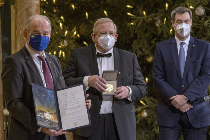 Archivo - 08 December 2020, Bavaria, Munich: German physicist Reinhard Genzel (C) shows the medal for her Nobel Prize in Physics, after receiving it with the certificate in advance from Sweden's ambassador Per Thoeresson (L). The traditional award cerem