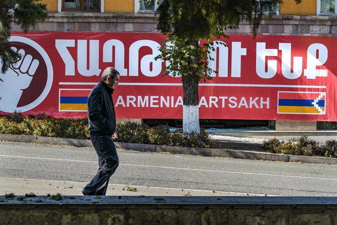 Archivo - Un hombre camina por una calle de Stepanakert, capital de Nagorno Karabaj, cerca de un cartel con la bandera armenia y de Artsaj, como se conoce en Armenia a Nagorno-Karabaj