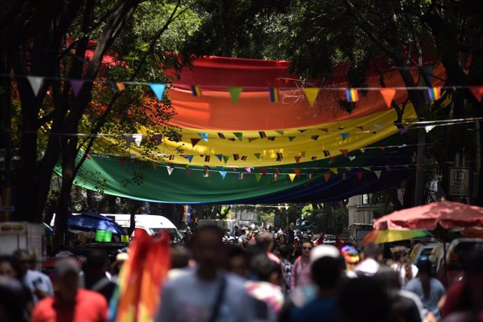Archivo - La gente camina bajo una gran bandera arcoíris durante el Desfile del Orgullo LGBT en Ciudad de México 2019. 