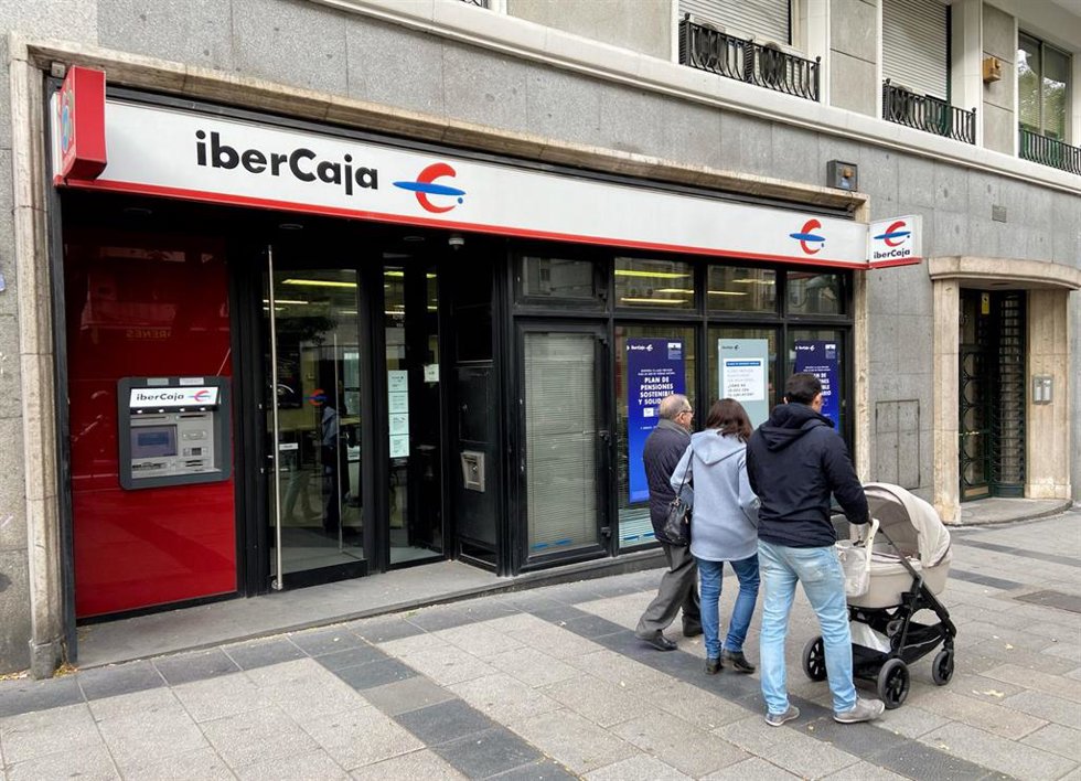 Archivo - Una familia pasea junto a una oficina de IberCaja en Madrid.