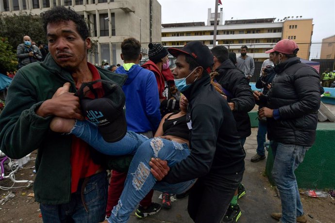 24 September 2021, Chile, Iquique: Migrants carry a woman who fainted during an operation by security forces. Security forces evicted migrants from a place where they were living in tents. Photo: Cristian Vivero Boornes/Agencia Uno/dpa