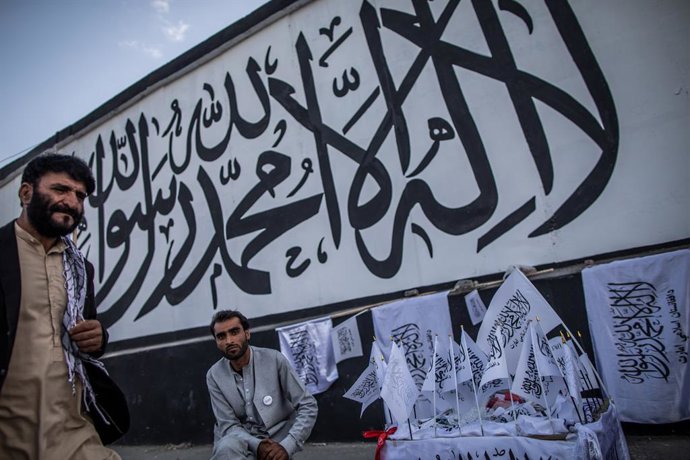 24 September 2021, Afghanistan, Kabul: An Afghan man sells Taliban flags backdropped by the Muslim creed written on a wall of the former United States embassy in Kabul. Photo: Oliver Weiken/dpa