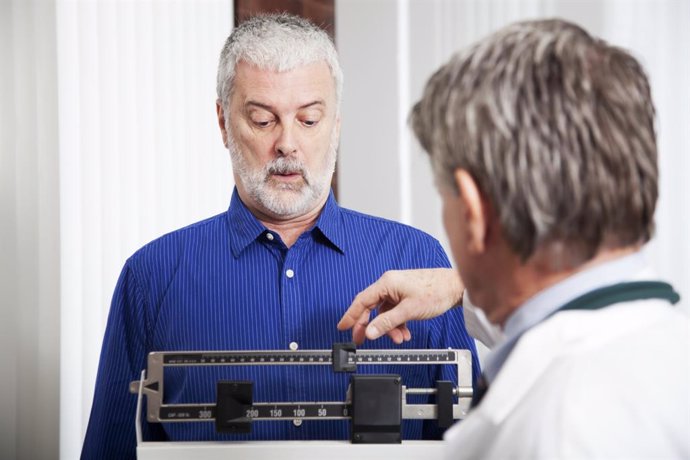 Archivo - Hombre pesándose en una báscula en la consulta del médico.