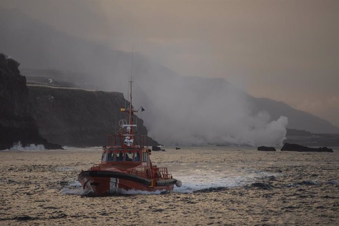 Un barco navega cerca de la columna de humo y la lava del volcán de Cumbre Vieja a su llegada al Océano Atlántico