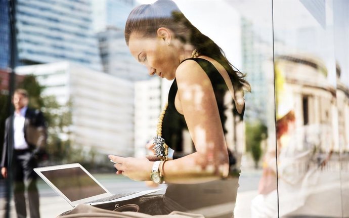 Archivo - Mujer conectada a WiFi con un ordenador y un móvil.
