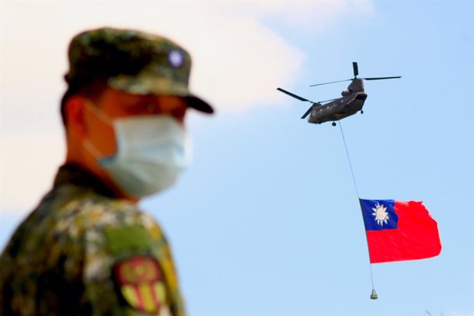 28 September 2021, Taiwan, Taoyuan: A soldier stands guard as a Chinook Helicopter carrying a tremendous Taiwan flag flies over a military camp, as part of a rehearsal for the flyby performance for Taiwan's Double-Ten National Day Celebration. The 18-me