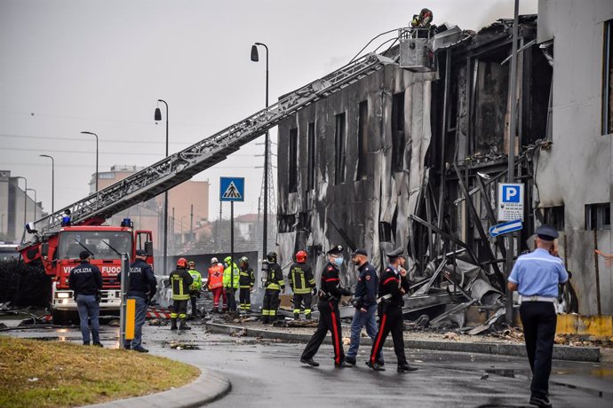 03 October 2021, Italy, Milan: Policemen and firefighters inspect the damage at the scene where a light airplane crashed into an empty office building. According to Italian media reports, the pilot and all five passengers were killed in the accident. Ph