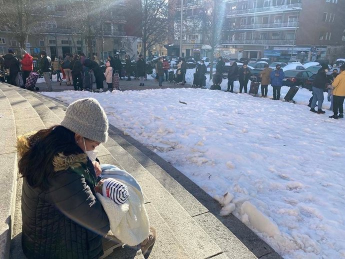 Archivo - Una madre con su hijo junto a una cola de personas para recibir ayuda.