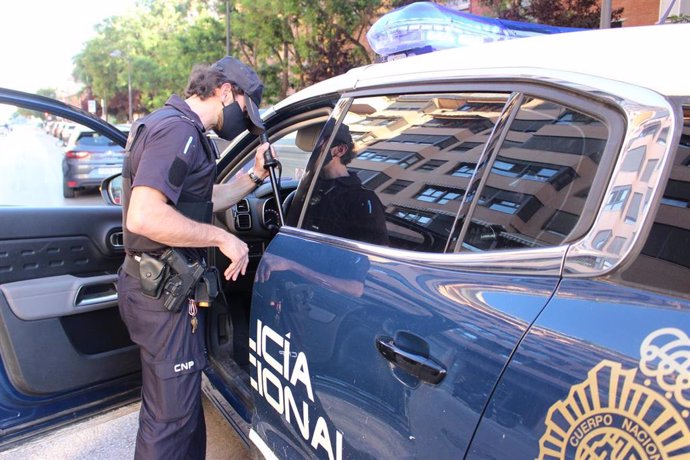 Un agente de Policía Nacional junto a un coche patrulla.