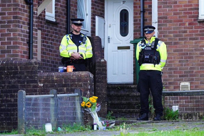 Archivo - 16 August 2021, United Kingdom, Plymouth: Police officers stand near floral tributes left outside 17 Biddick Drive in the Keyham area of Plymouth, where five people were killed by gunman Jake Davison in a firearms incident on Thursday evening.