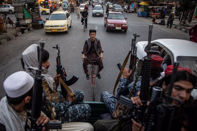 22 September 2021, Afghanistan, Kabul: An Afghan man rides a bicycle as young Taliban fighters patrol the streets of Kabul on the back of a pick up truck. Photo: Oliver Weiken/dpa