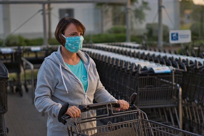 Archivo - Mujer a la salida de un supermercado con carro de la compra. Mascarilla de tela.