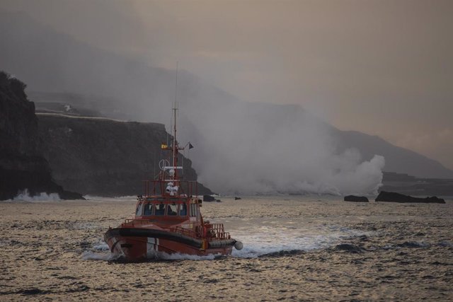 Un barco navegando cerca de la columna de humo y la lava del volcán de Cumbre Vieja a su llegada al Océano Atlántico