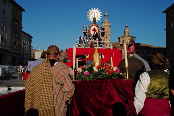 Varias personas vestidas con los tradicionales trajes de maño se dirigen a la Basílica del Pilar para realizar la ofrenda de flores a la Virgen del Pilar en Zaragoza.