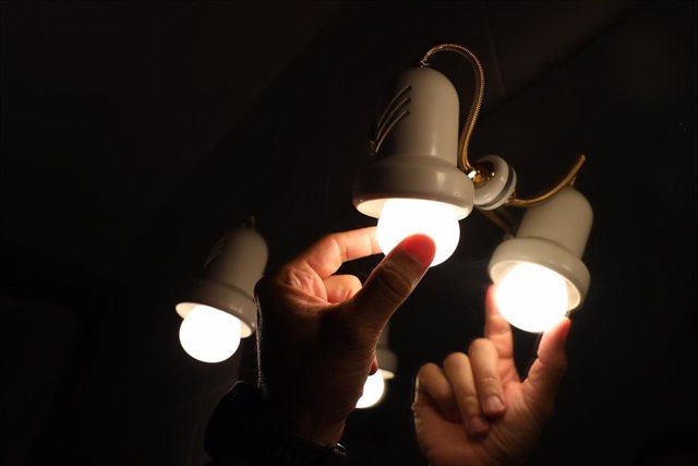 Archivo - Una persona cambia la bombilla de una lámpara
