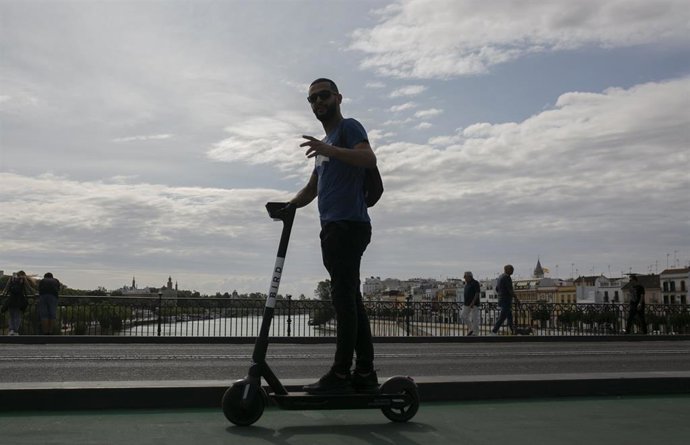 Archivo - Un joven atraviesa el Puente de Triana de Sevilla con patinete eléctrico