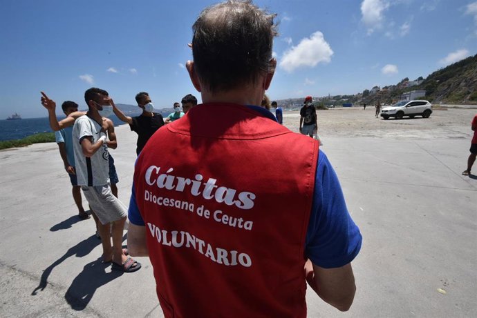 Archivo - Un trabajador de Cáritas Diocesana reparte alimentos a migrantes que entraron a Ceuta.