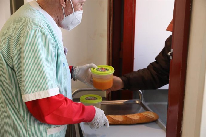 Archivo - Un voluntario (i) trae comida a una persona (d) como parte del reparto diario de alimentos de un comedor social, foto de archivo